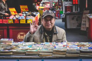 Marchand asiatique qui fait un signe avec sa main devant une table avec des catalogues.